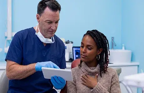 Dentist in blue scrubs reviewing digital treatment records on a tablet with a female patient at R&S Dental Associates in Clifton, NJ.